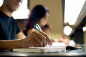 man writing on notebook with pen