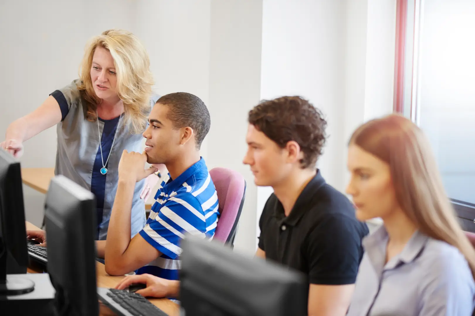 Teacher helping students with computers.