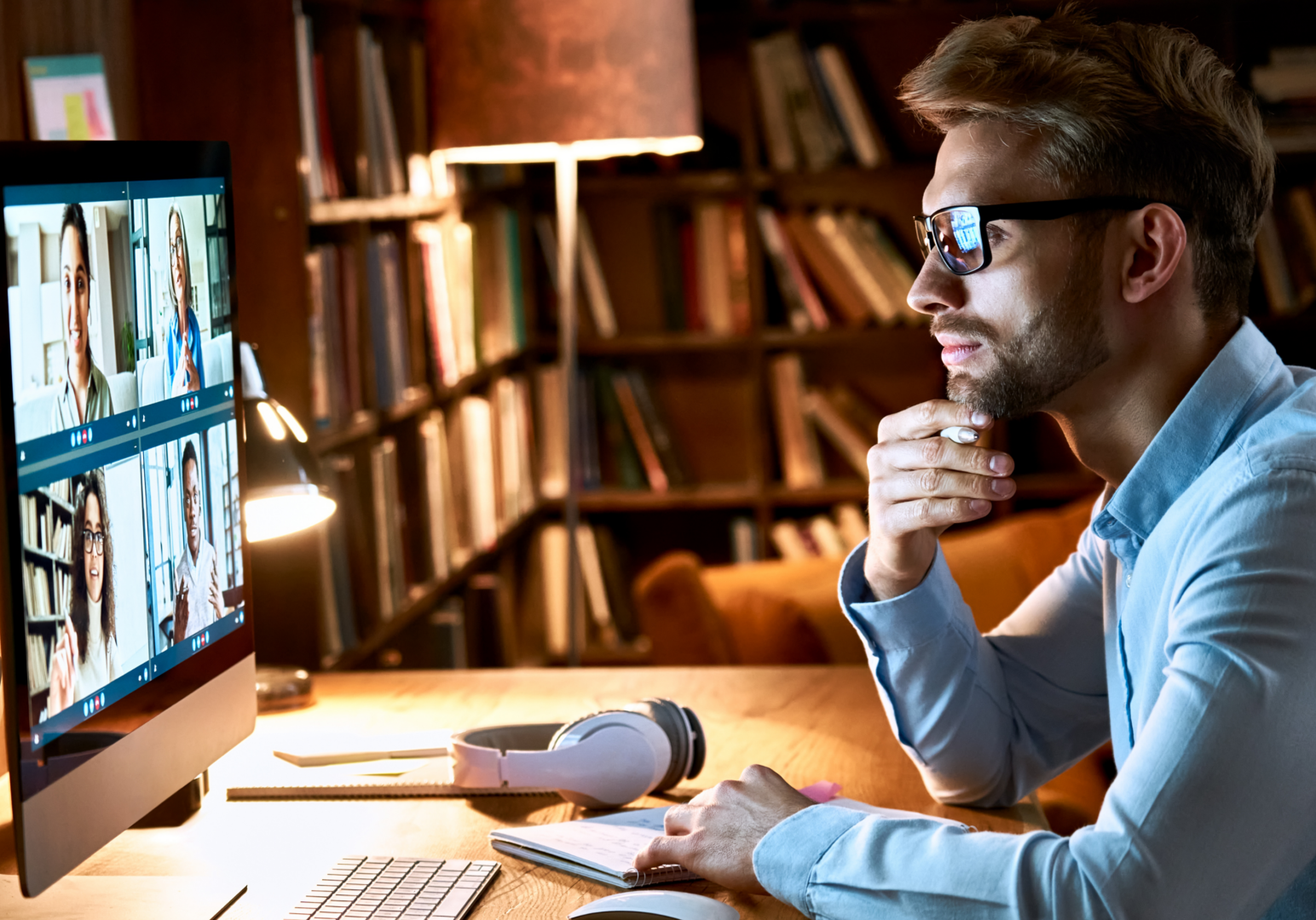 Man in glasses looking at multiscreen video call.