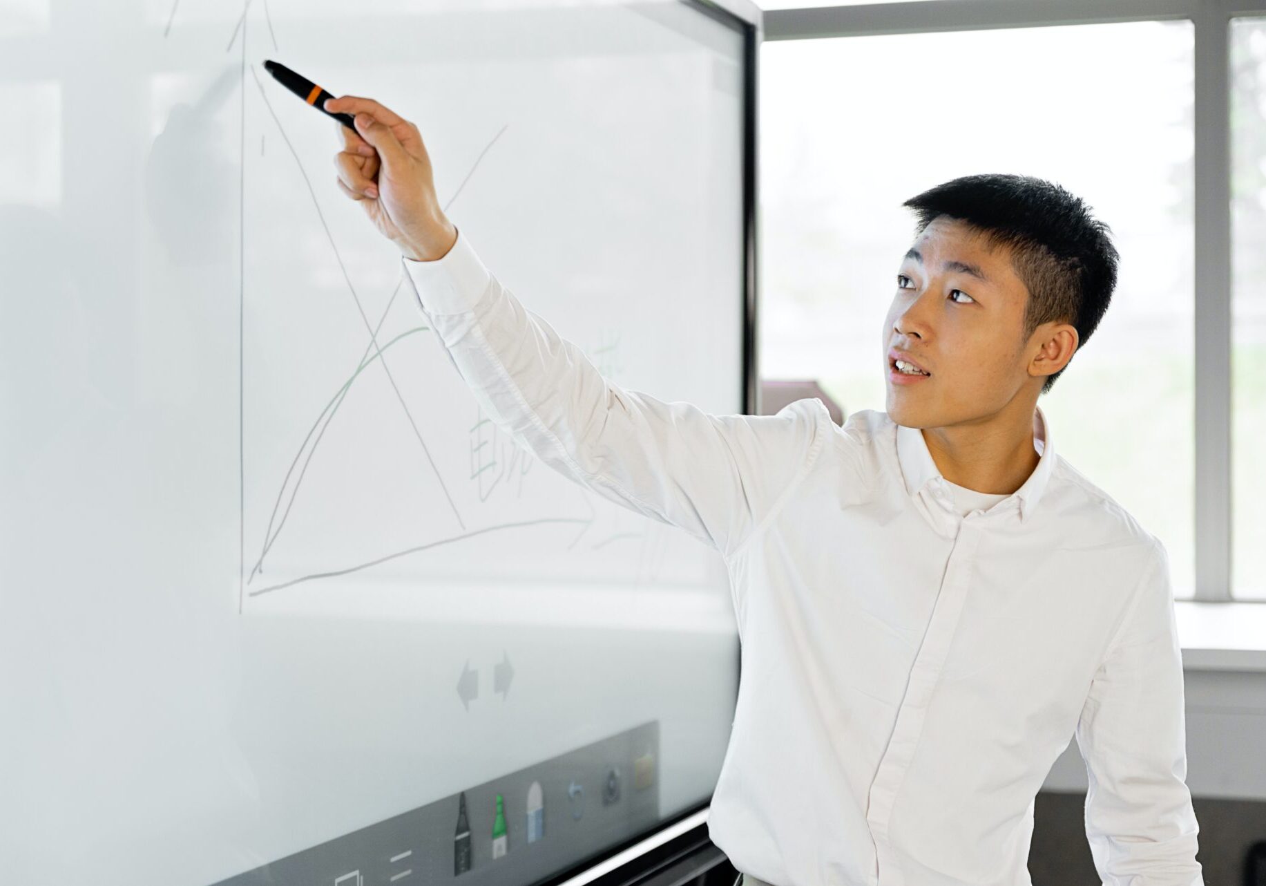 Young Asian man drawing graph on whiteboard.